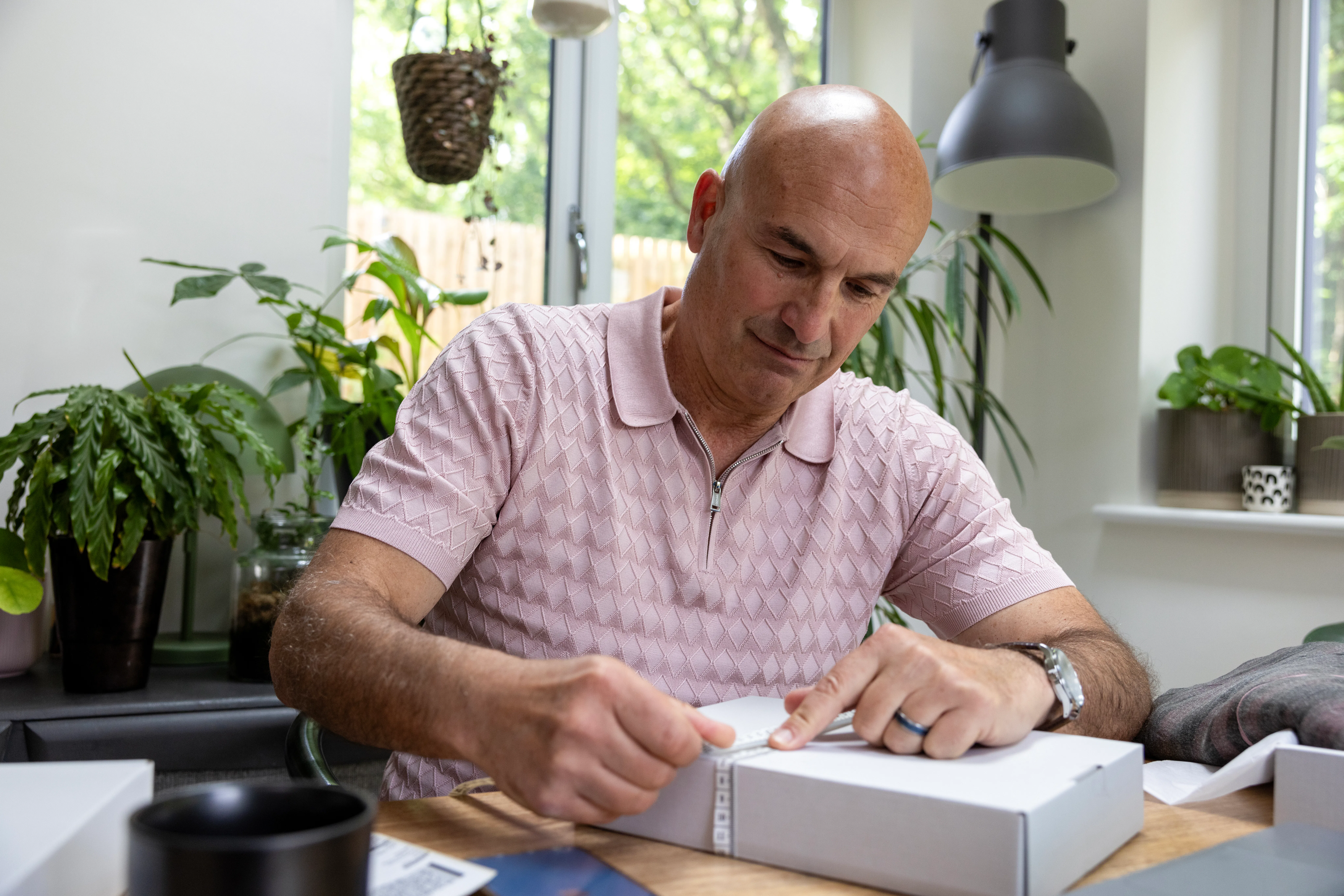 Customer sat at a desk holding a tape measure with their index finger to measure the size of their parcel.