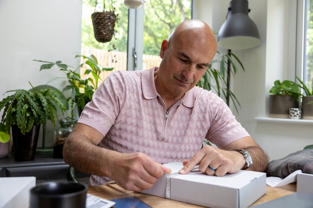 Customer sat at a desk holding a tape measure with their index finger to measure the size of their parcel.
