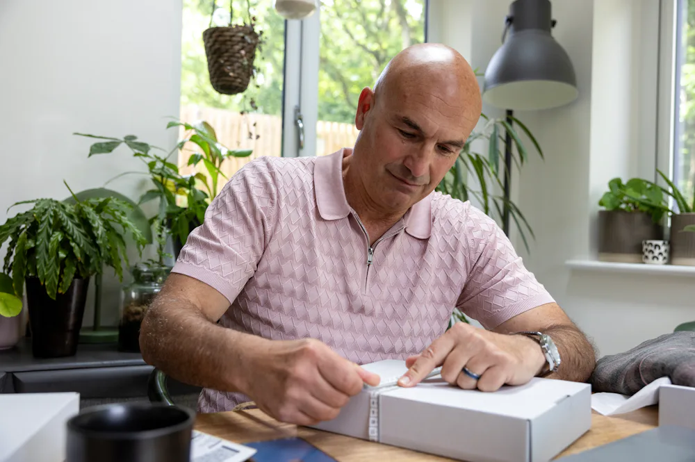 Customer sat at a desk holding a tape measure with their index finger to measure the size of their parcel.