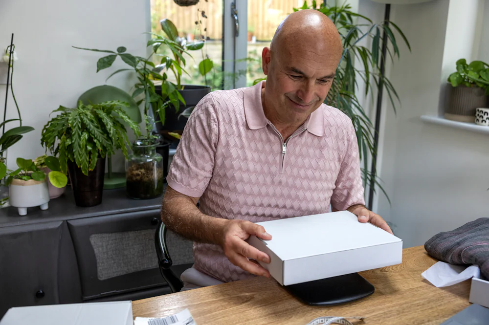 Customer sat at a desk holding their parcel and placing onto a set of digital weighing scales.