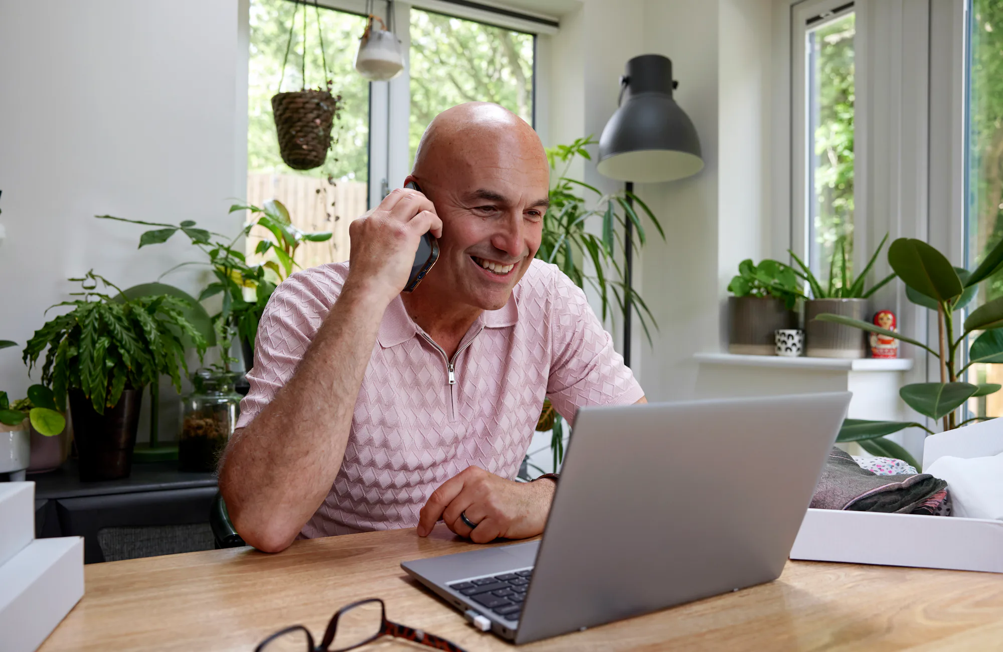 Customer sat at a desk in their office taking a phone call and looking at a laptop.