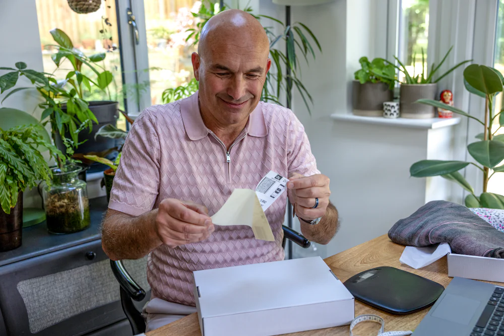 Customer sat at a desk unpeeling a printed delivery label to place onto the parcel in front of them.