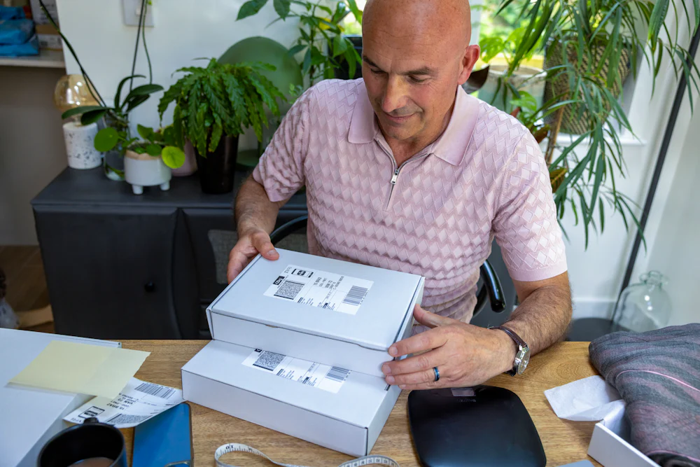 Customer sat at a desk holding two parcels that have been packaged and labelled, glancing down at them.
