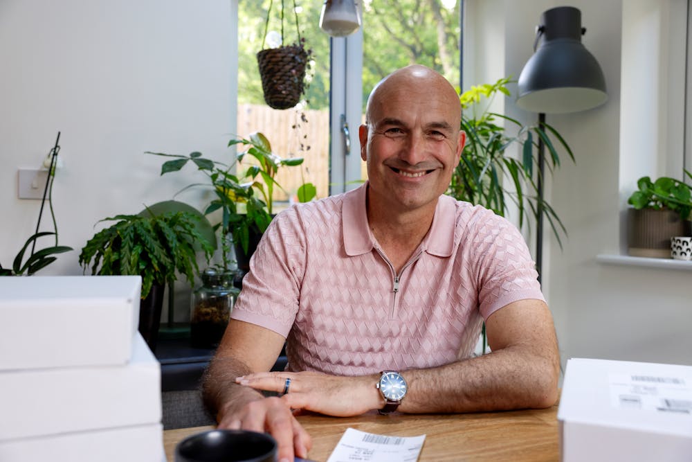 Customer sat at a desk posing for a photo and smiling. Multiple parcels are shown in the foreground.
