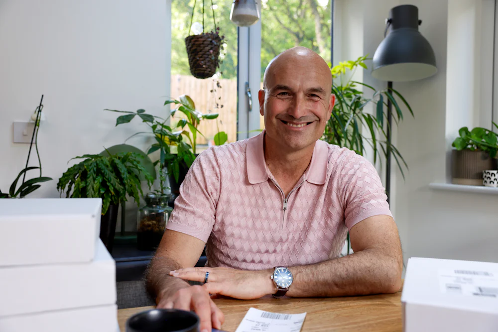 Customer sat at a desk posing for a photo and smiling. Multiple parcels are shown in the foreground.