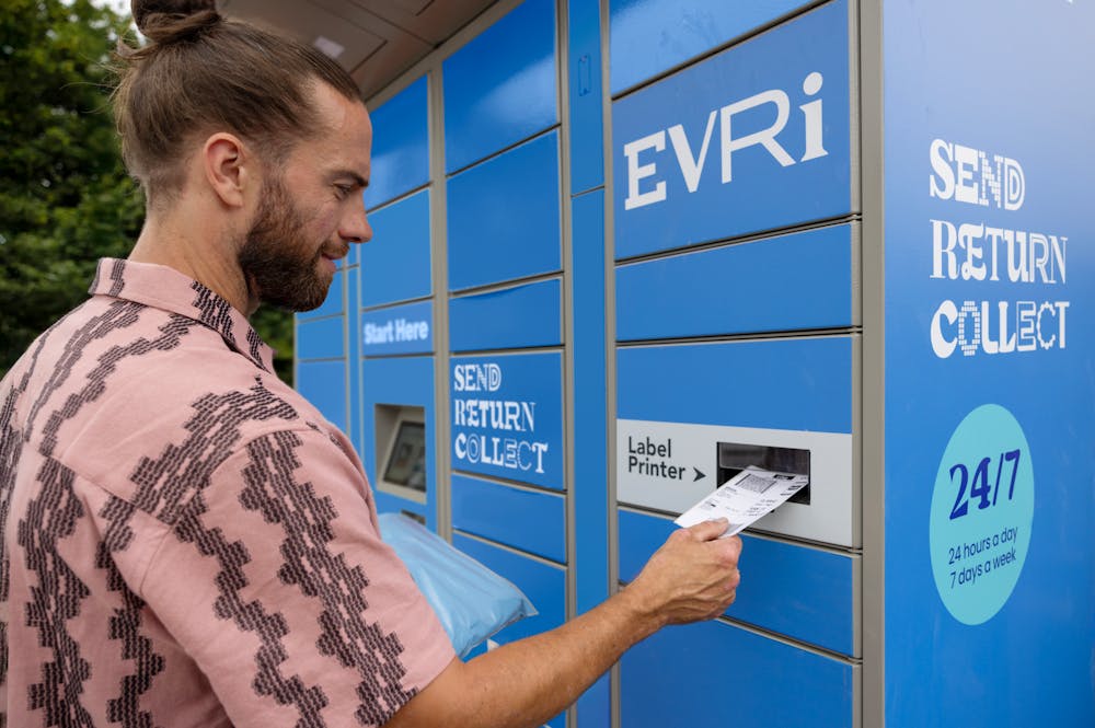 Customer holding parcel and standing outside at an Evri Locker, watching as their label prints out