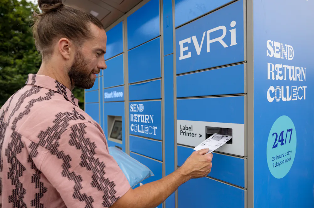 Customer holding parcel and standing outside at an Evri Locker, watching as their label prints out