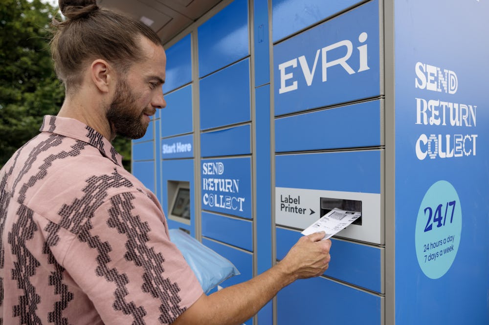 Customer holding parcel and standing outside at an Evri Locker, watching as their label prints out