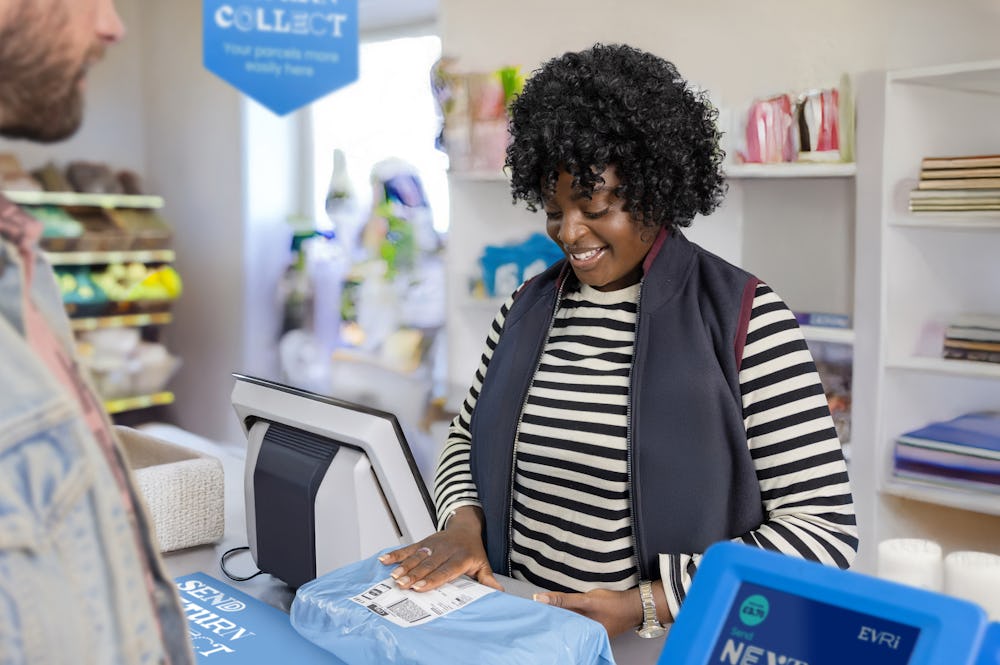 ParcelShop store assistant is glancing down and sticking a label onto the customer's parcel whilst smiling