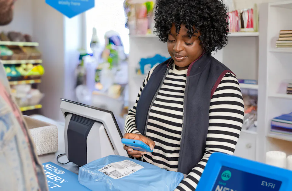 ParcelShop store assistant is holding a blue hand-held device to scan the customer's parcel.