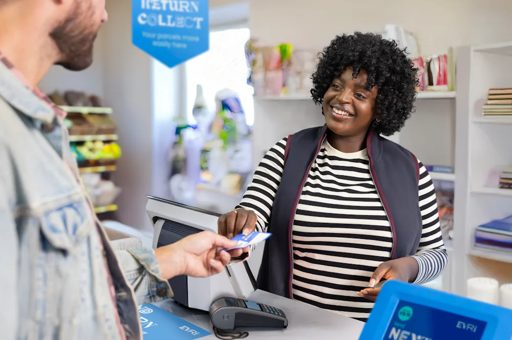 ParcelShop store assistant is smiling and handing a blue receipt to the customer to confirm their parcel has been accepted.
