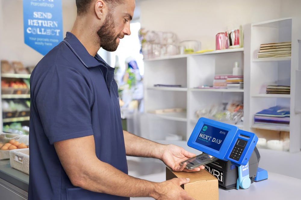 Customer in a ParcelShop store scanning their parcel's QR code using a Print in Store device to print their label for sending.