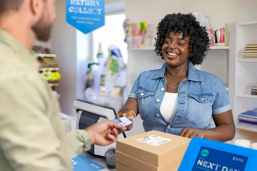 ParcelShop store assistant is smiling and handing a blue receipt to the customer to confirm that their parcels have been accepted.