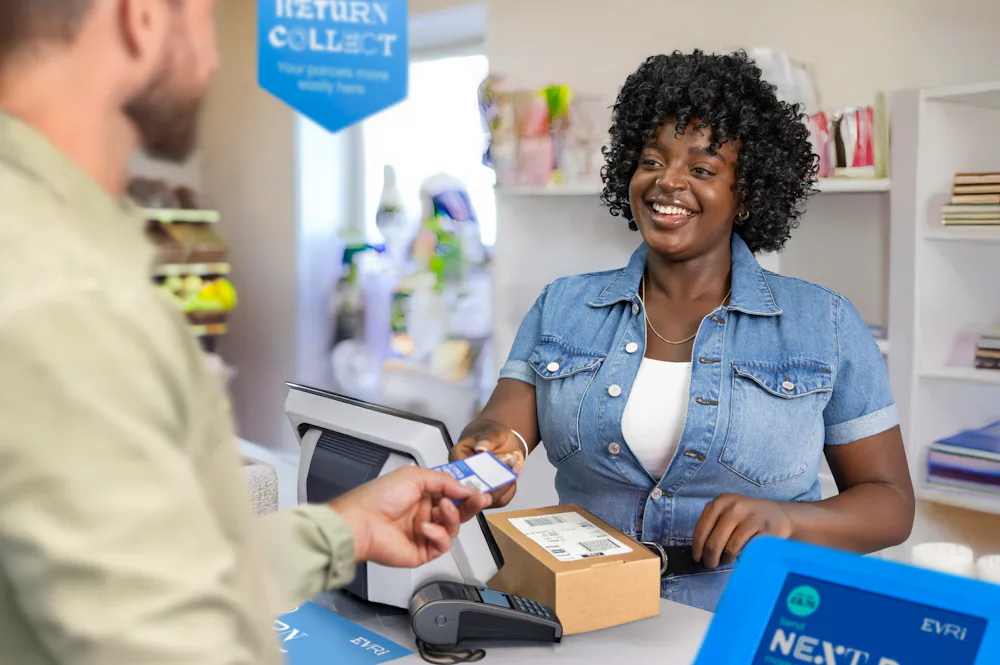 ParcelShop store assistant is smiling at the customer and handing a blue receipt to confirm that their parcel has been accepted.