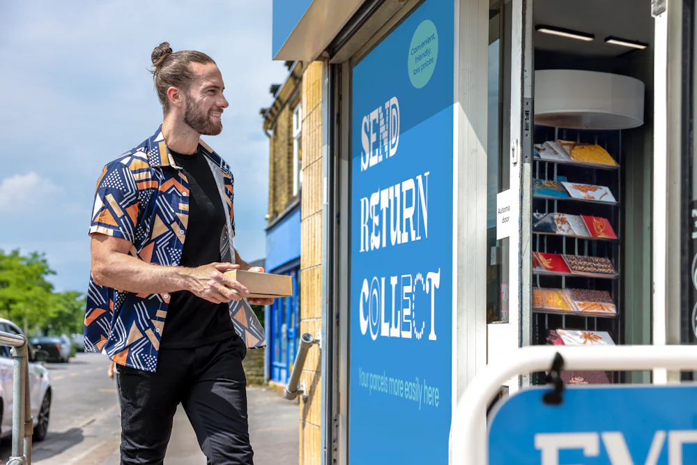 Customer stood outside of a ParcelShop store smiling and holding a parcel. The blue Evri signage can be seen on the storefront.