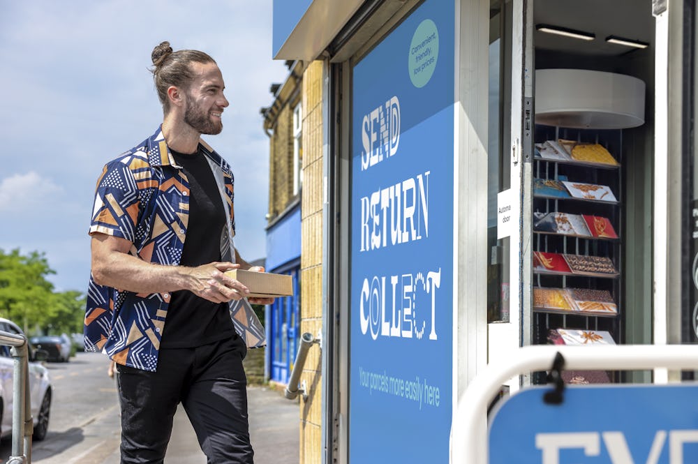 Customer stood outside of a ParcelShop store smiling and holding a parcel. The blue Evri signage can be seen on the storefront.