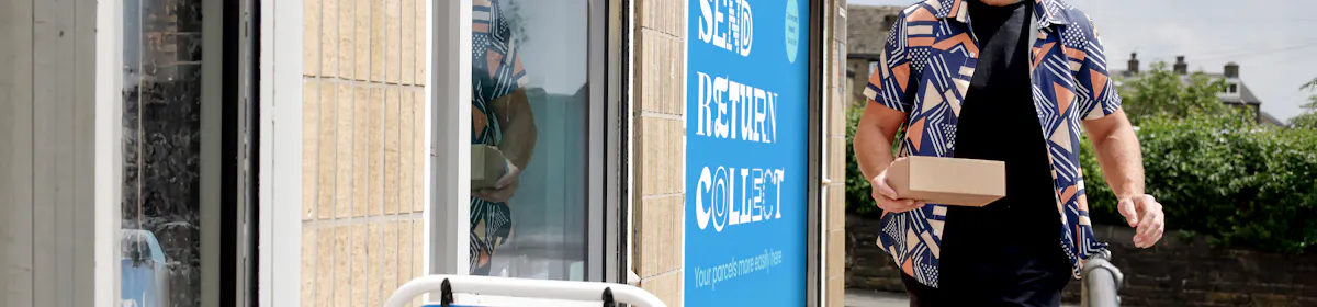 Customer walking towards a ParcelShop store holding a parcel. The blue Evri signage can be seen on the storefront with a free-standing sign near the entrance.