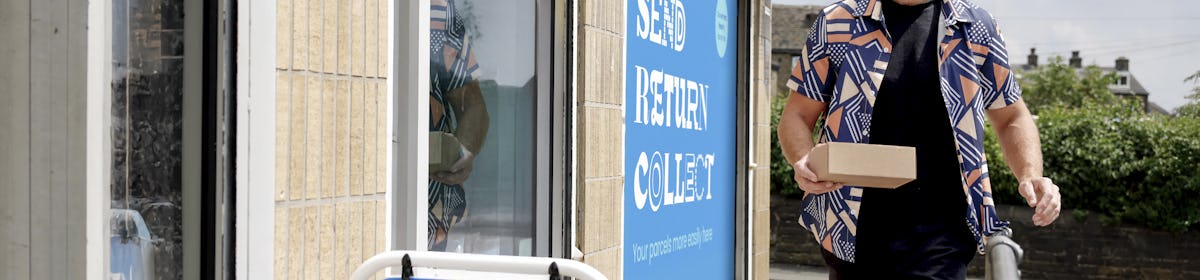 Customer walking towards a ParcelShop store holding a parcel. The blue Evri signage can be seen on the storefront with a free-standing sign near the entrance.