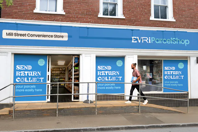 An Evri ParcelShop is in full view with its blue signage and a customer is walking up the accesssbility ramp and holding a parcel.