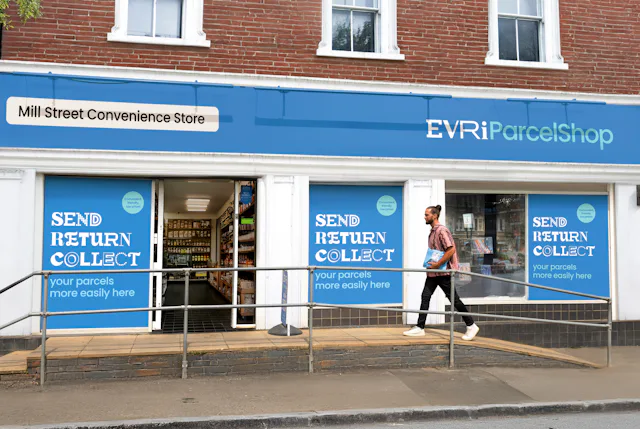 An Evri ParcelShop is in full view with its blue signage and a customer is walking up the accesssbility ramp and holding a parcel.