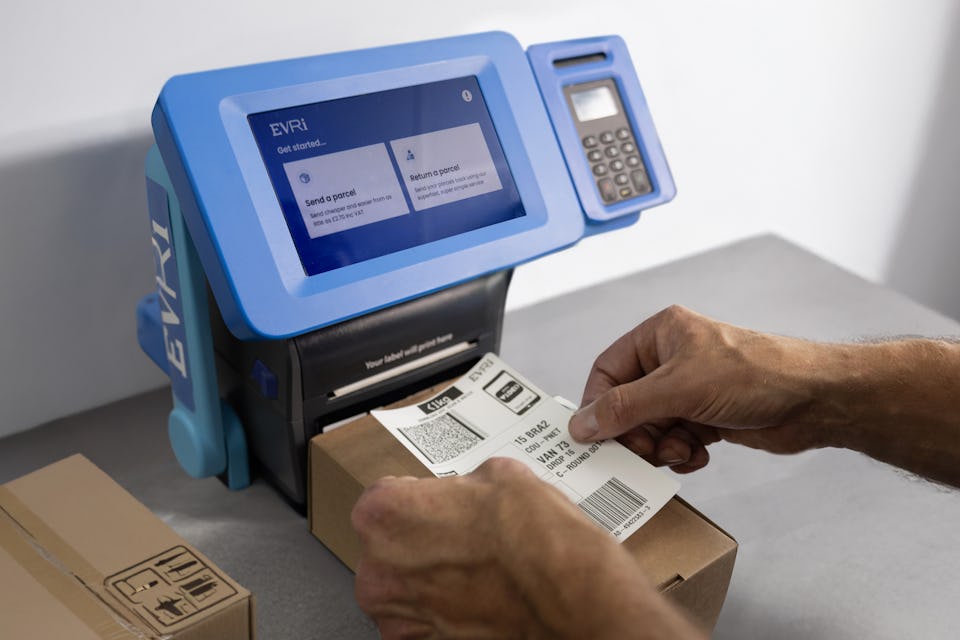 A close-up of a customer applying a label to their parcel. A ParcelShop Print in Store device is in view behind the parcel.