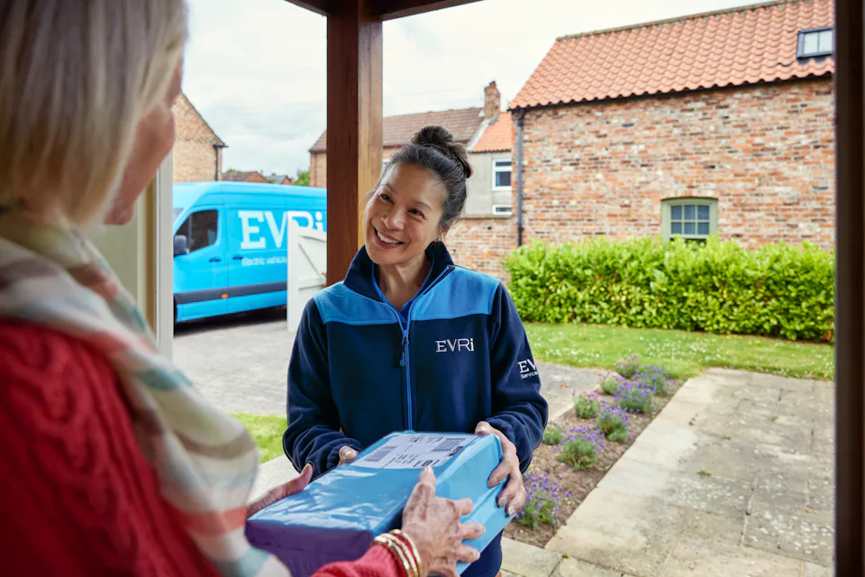 A female courier hands a parcel to a recipient. They are both examining the parcel.