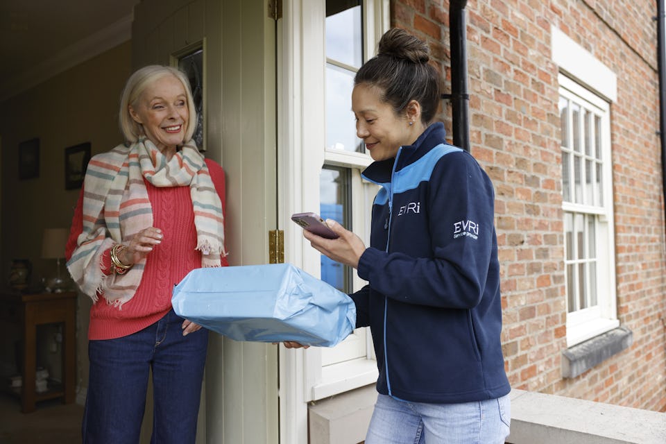Female courier handing parcel to recipient. She is taking a proof of delivery photo.