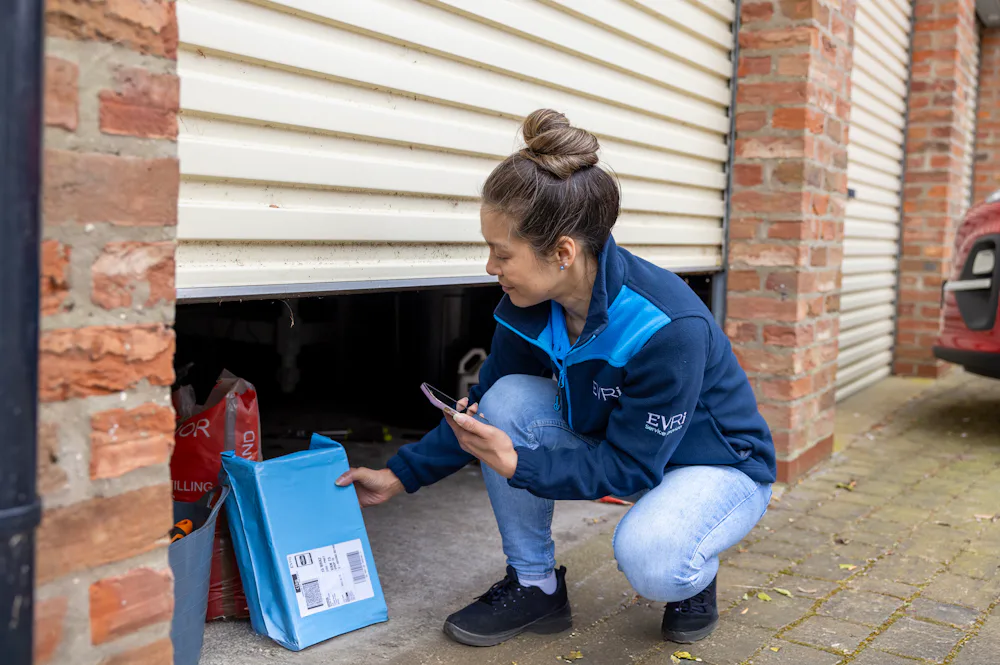 A courier is outside next to an open garage door, carefully placing a parcel inside the garage as a safe place location.