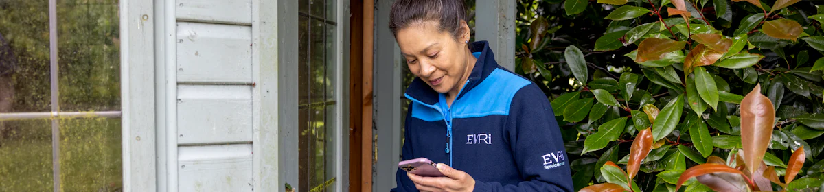 A courier is outside next to a summer house, scanning a parcel for its delivery to a safe place.