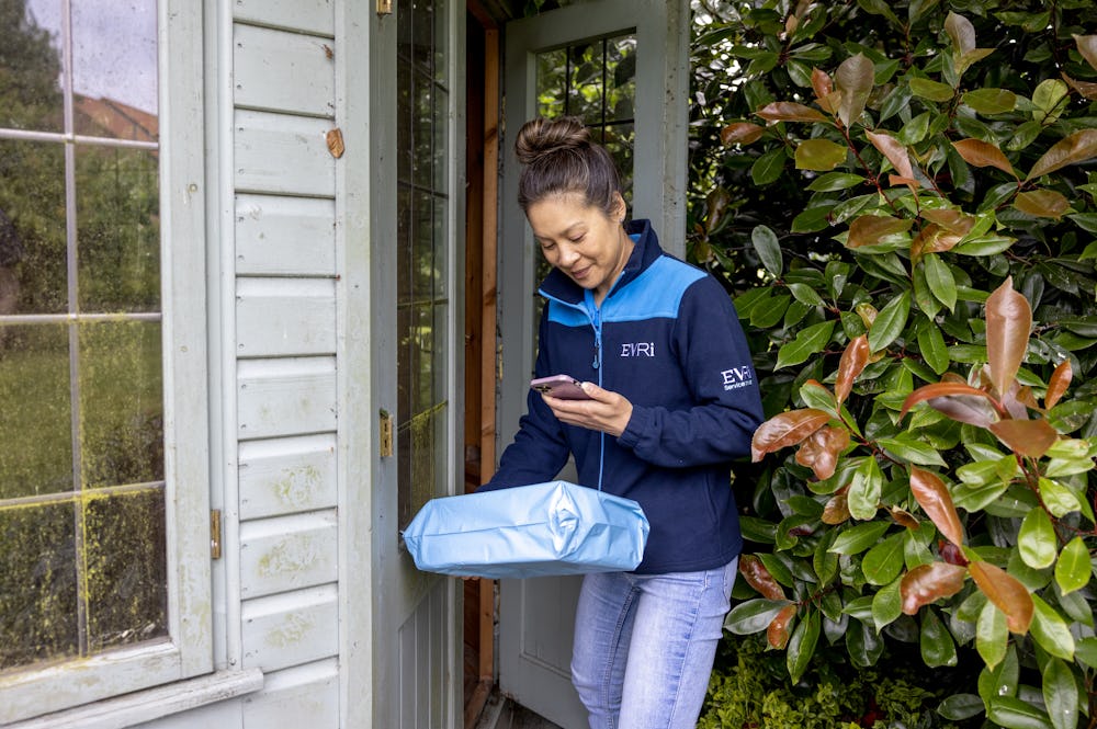 A courier is outside next to a summer house, scanning a parcel for its delivery to a safe place.