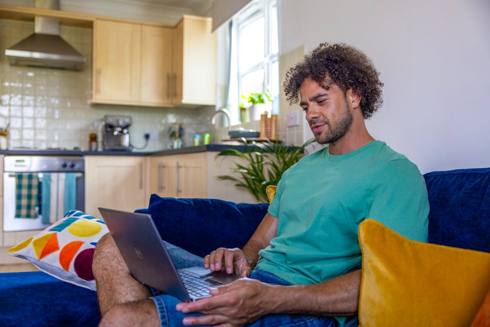 A side-view profile of a customer sitting on a sofa, with a laptop resting on their lap as they look down at the screen.