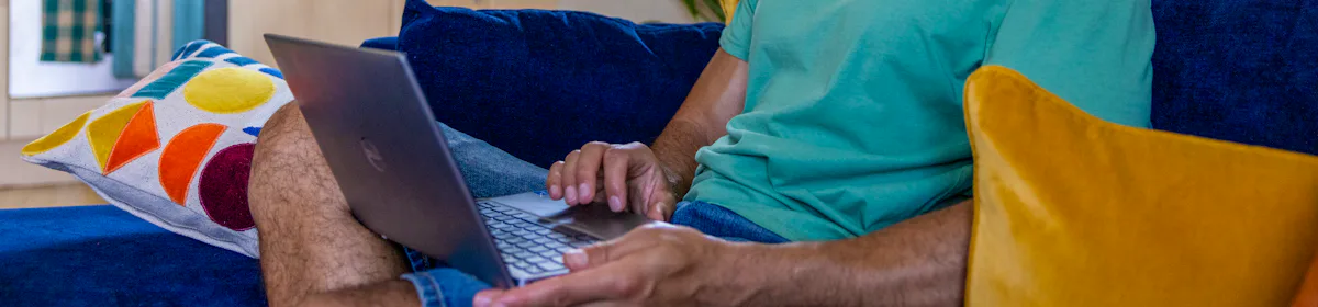 A side-view profile of a customer sitting on a sofa, with a laptop resting on their lap as they look down at the screen.