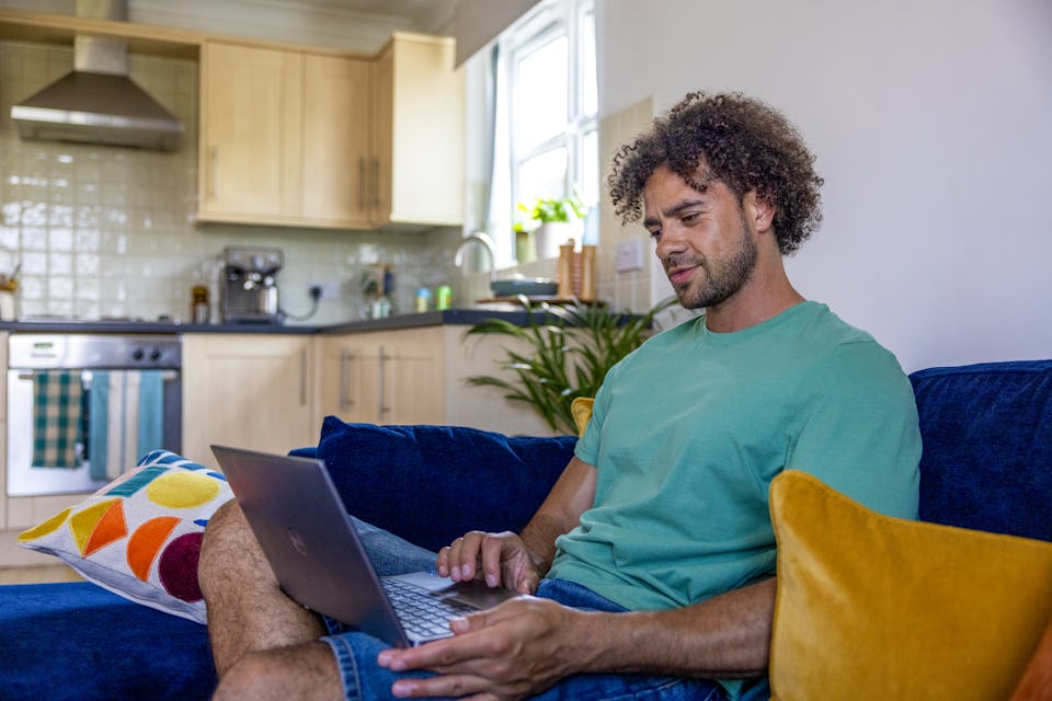 A side-view profile of a customer sitting on a sofa, with a laptop resting on their lap as they look down at the screen.