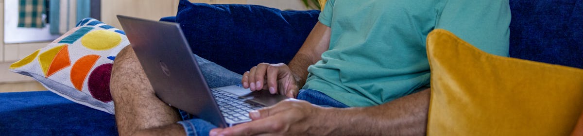 A side-view profile of a customer sitting on a sofa, with a laptop resting on their lap as they look down at the screen.