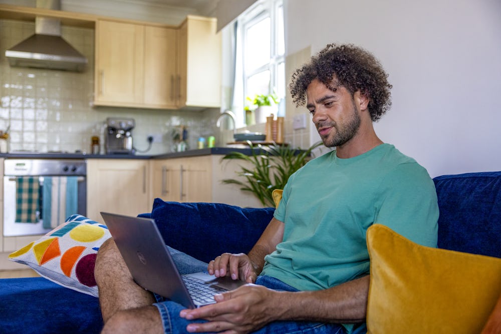 A side-view profile of a customer sitting on a sofa, with a laptop resting on their lap as they look down at the screen.