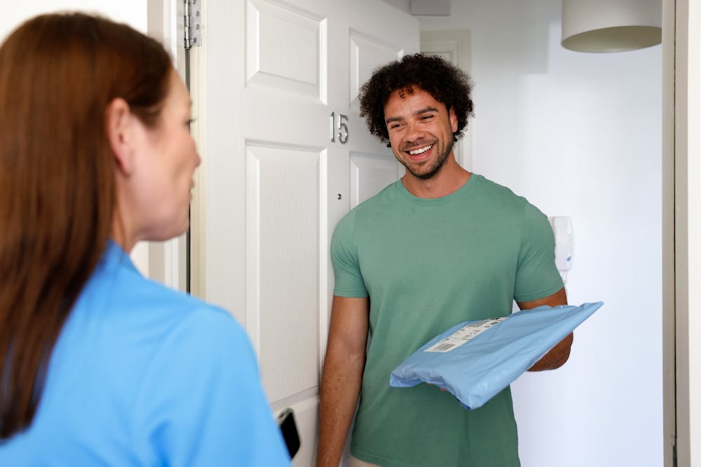 A customer is standing in the doorway of their home, holding their parcels and smiling. The courier can be seen facing towards the customer in a friendly conversation.