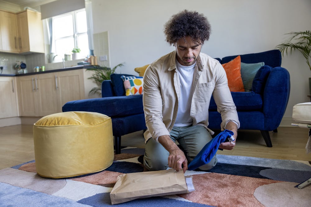 A customer is crouched on the floor of their apartment, holding recyclable packaging in one hand and items in another.