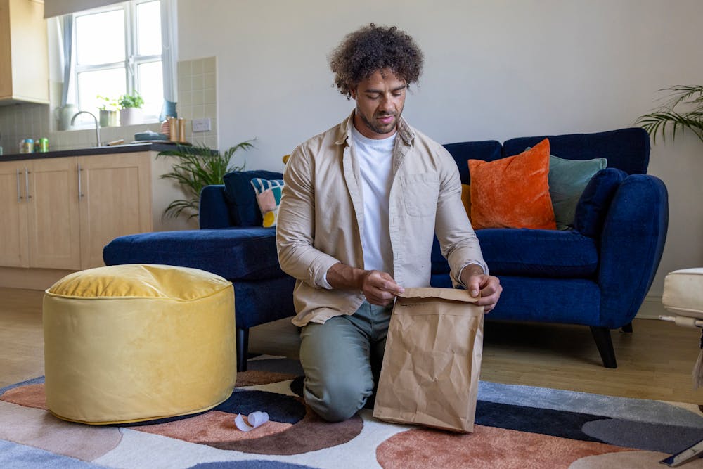 A customer is crouched on the floor of their apartment, sticking down the seal of their recyclable packaging.