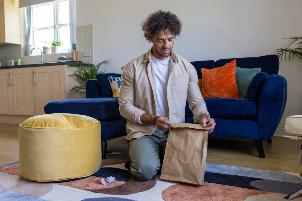 A customer is crouched on the floor of their apartment, sticking down the seal of their recyclable packaging.