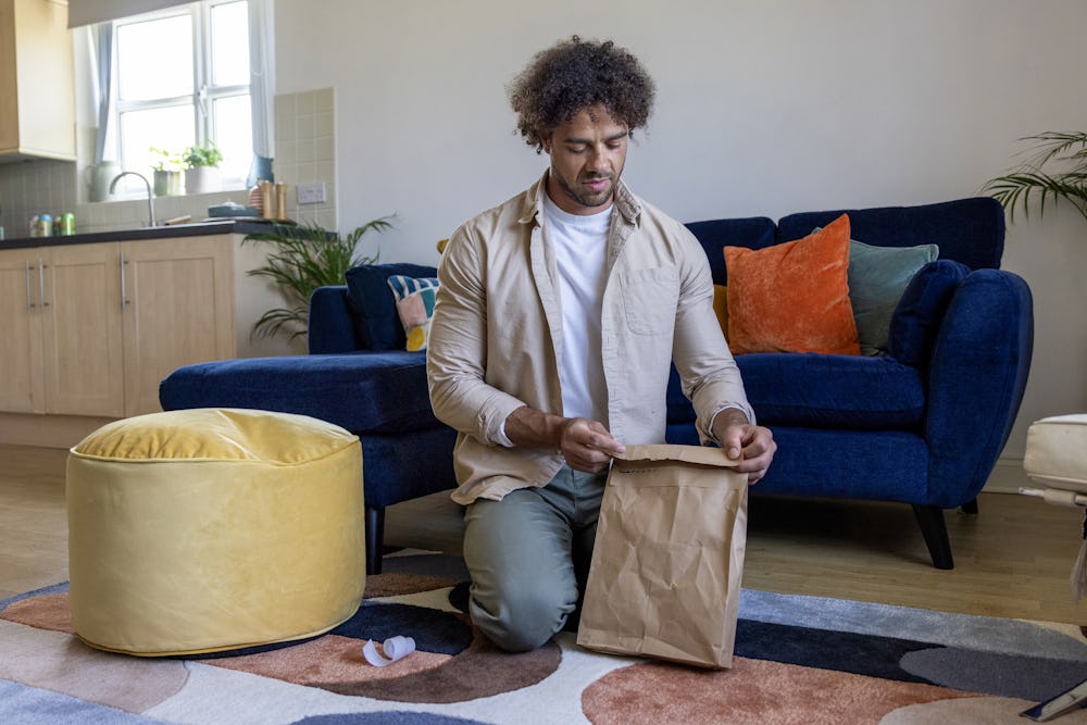 A customer is crouched on the floor of their apartment, sticking down the seal of their recyclable packaging.