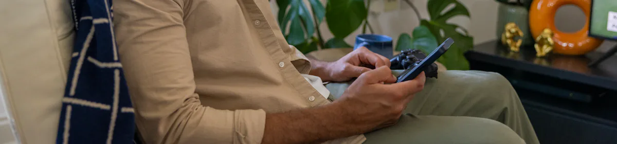 A side-profile view of a customer sitting on a sofa in their lounge, holding their mobile phone and looking at their screen.