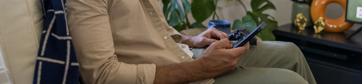 A side-profile view of a customer sitting on a sofa in their lounge, holding their mobile phone and looking at their screen.