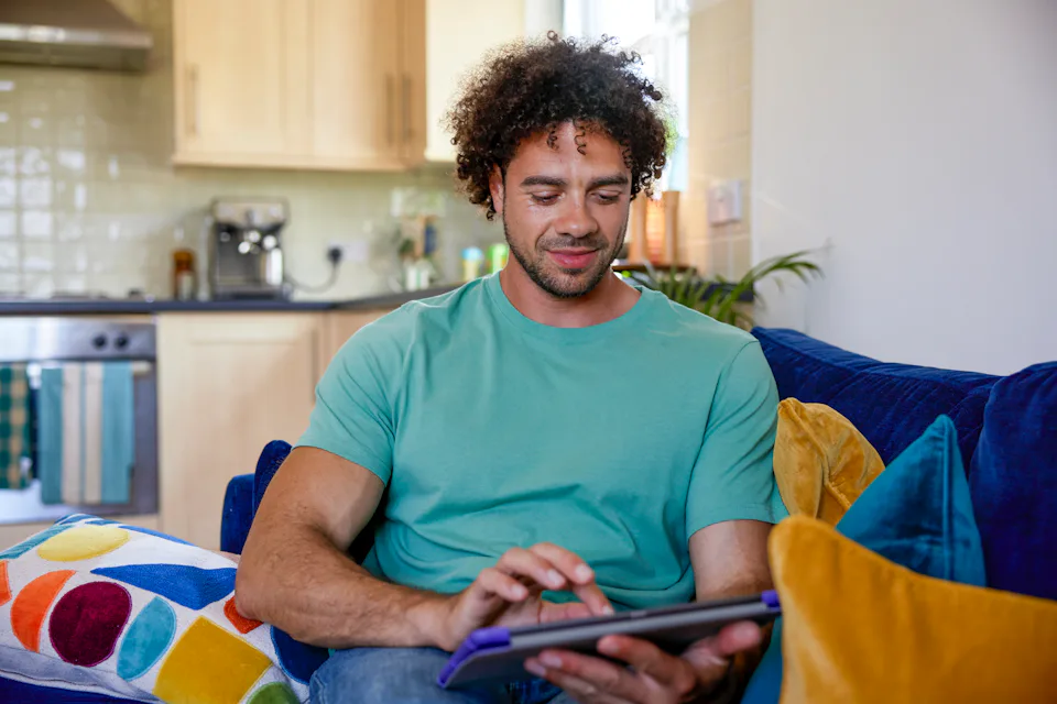 A customer sat on a sofa in their lounge, holding their tablet and looking at their screen.
