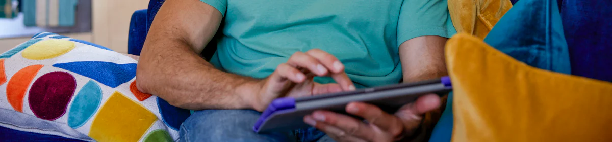 A customer sat on a sofa in their lounge, holding their tablet and looking at their screen.