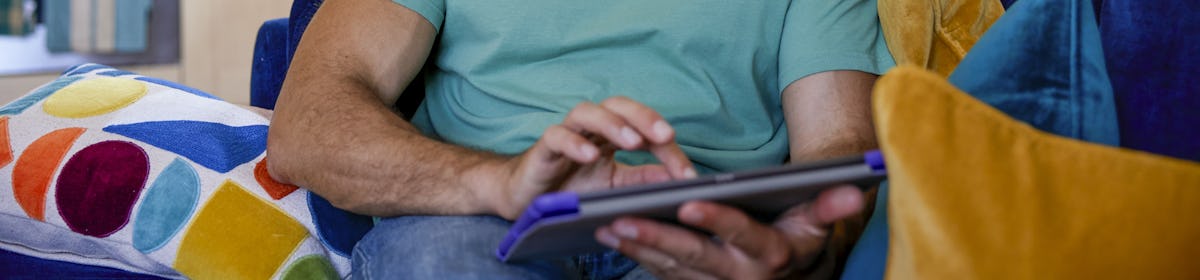 A customer sat on a sofa in their lounge, holding their tablet and looking at their screen.