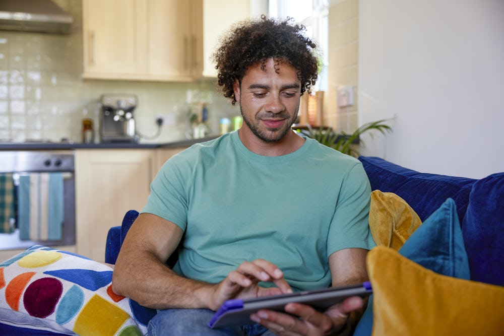 A customer sat on a sofa in their lounge, holding their tablet and looking at their screen.