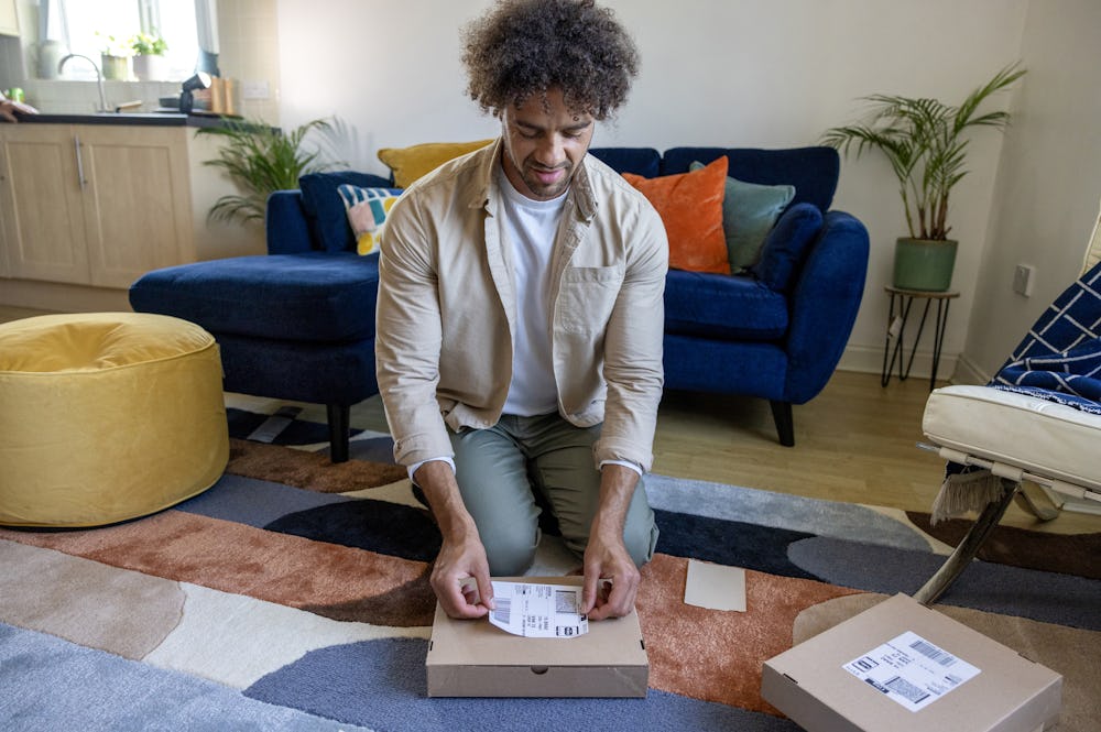 A customer is crouched on the floor of their apartment, placing their label on the parcel in front of them.