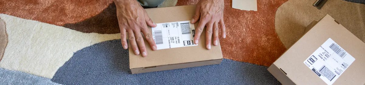 A close-up of a customer's hands as they are crouched on the floor, applying a label to their parcel. They are surrounded by lots of parcels.