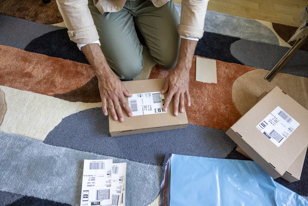A close-up of a customer's hands as they are crouched on the floor, applying a label to their parcel. They are surrounded by lots of parcels.