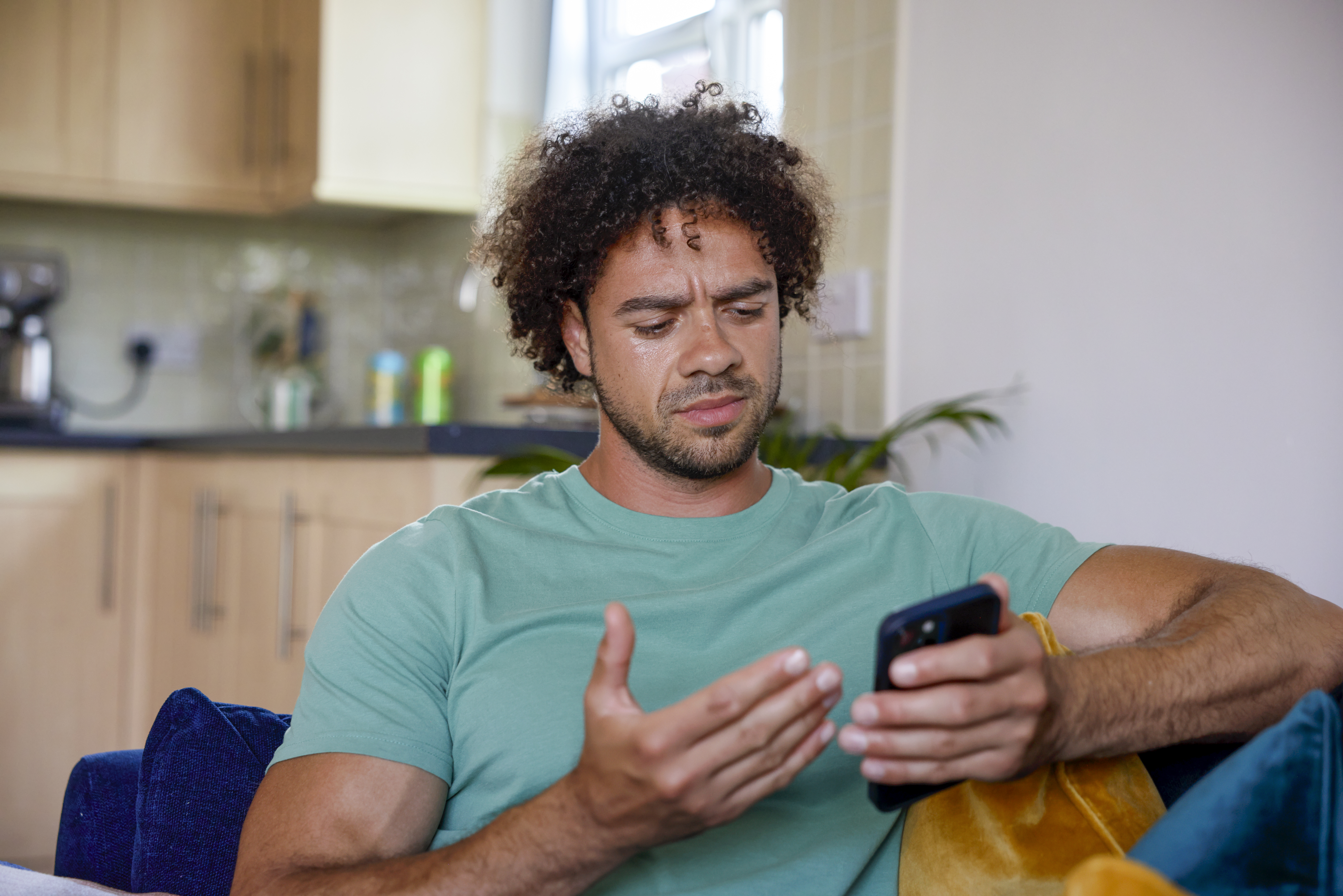 A close-up of a customer sitting on a sofa, holding their phone and looking confused at their screen.
